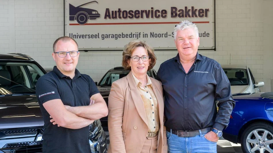 Autoservice Bakker historie: drie personen tussen auto's bij een autobedrijf noord-scharwoude